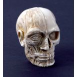 A 19th century carved ivory memento mori study of a skull, one half of the face exposing flesh and