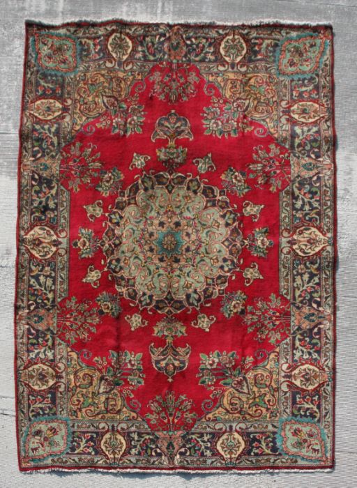 A Persian Tabriz woollen hand made rug with with central foliate gul within floral borders, on a red