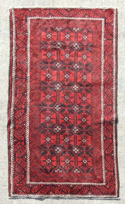 A Persian Baluch woollen hand made rug with repeated guls within a stylised border, on a red ground,