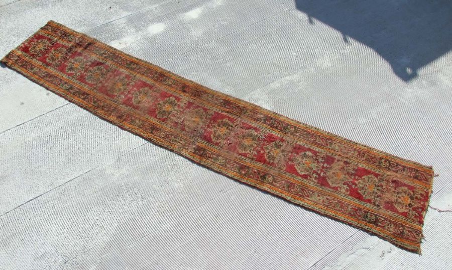 A Turkish runner with repeated floral decoration on a red ground, 392 by 73cms.