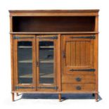 An Arts & Crafts oak side cabinet, the pair of glazed doors enclosing a shelved interior flanked