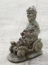 A reconstituted stone garden figure of a gnome riding in a car. 53cm high