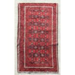 A Persian Baluch woollen hand made rug with repeated guls within a stylised border, on a red ground,