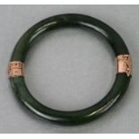 A yellow metal mounted (tests as gold) opening dark green figured jade bangle, 7.5cms dimeter.