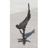 A large floor standing bronze figure of a macaw parrot perched on a tree stump with tail raised,