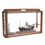 A diorama depicting a trawler, lighthouse and buildings, cased, 65cms wide.