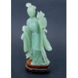 A Chinese green hardstone figure depicting a robed lady holding a fan, on a hardwood stand, 35cms