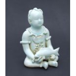 A Chinese pale celadon glaze figure depicting a seated child holding a fish, 20cms high.Condition