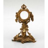 A rococo style gilt metal watch stand, 20cms high and 5cms diameter watch aperture.