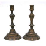A pair of 19th century bronze candlesticks with fluted columns over stepped wavy rimmed bases, 25cms