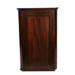 A 19th century mahogany corner cupboard, the panelled door enclosing a shaped shelved interior,