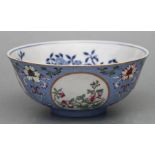 A Chinese blue, white and enamelled footed bowl decorated with flowers within roundels on a pale