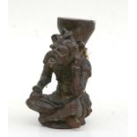 A carved wooden figure in the form of a jester sitting crossed legged, with traces of painted