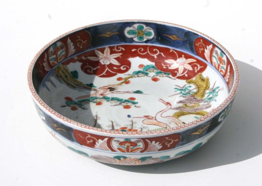 A Japanese Imari bowl decorated with birds in a river landscape, 25cms diameter together with a pair