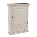 A painted pine wall cabinet with single panelled door enclosing a shelved interior, above three