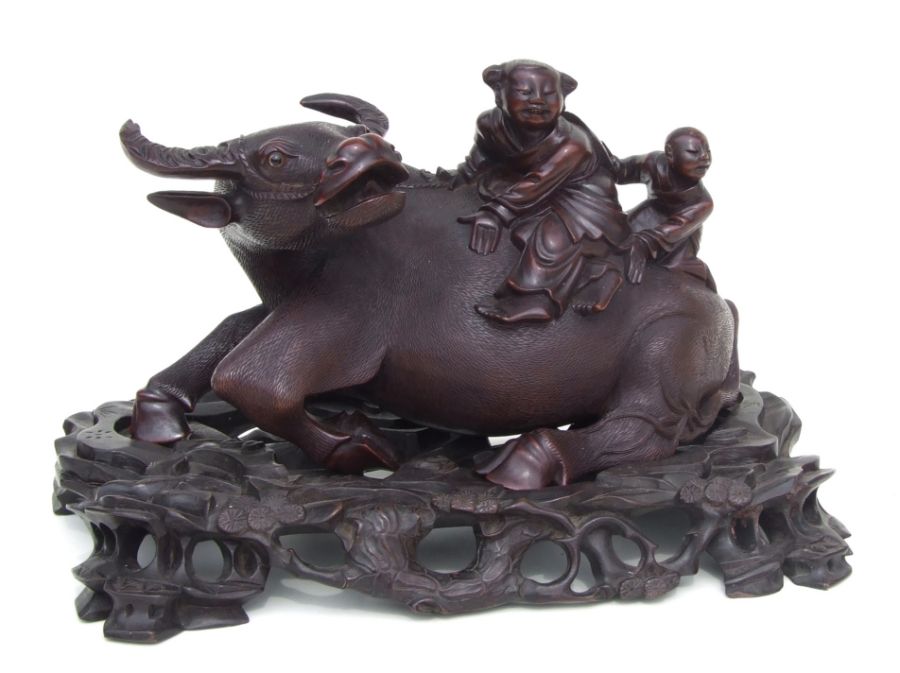 A Chinese hardwood carved group depicting a water buffalo with figures riding on its back, on a