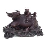A Chinese hardwood carved group depicting a water buffalo with figures riding on its back, on a