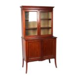 An Edwardian inlaid mahogany display cabinet on cupboard, the pair of glazed doors enclosing a