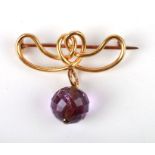 An Art Nouveau yellow metal brooch with amethyst coloured faceted drop.