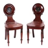 A pair of William IV mahogany hall chairs, the circular carved backs with armorial decoration
