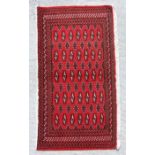 A small Persian Turkoman rug with repeat stylised design on a red ground, 130 by 60cms.