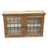 A stripped pine display cabinet, with a pair of leaded glass panelled doors enclosing a shelved