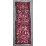 A Persian hand knotted woollen runner with repeated floral design, on a red ground, 280 by 75cms.