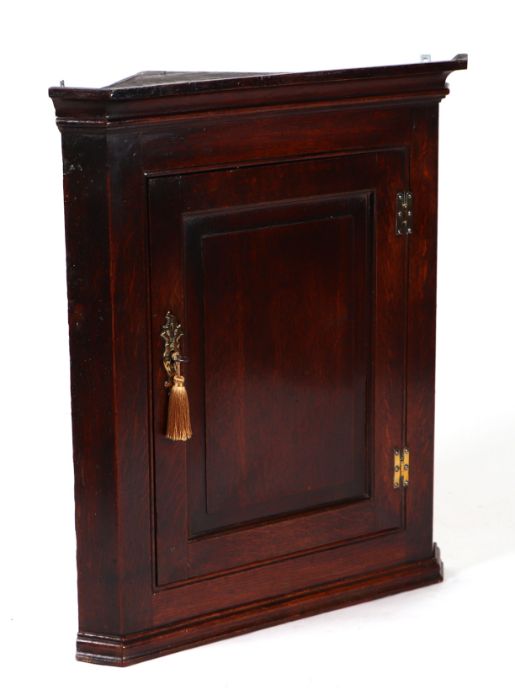 A George III oak hanging corner cupboard with single panelled door enclosing a shelved interior,