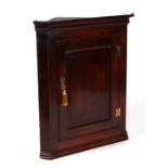 A George III oak hanging corner cupboard with single panelled door enclosing a shelved interior,