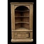 A large stripped pine corner open bookcase on cupboard, the moulded cornice above three shelves,