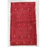 A small Persian Turkoman rug with repeat stylised design on a red ground, 130 by 70cms.