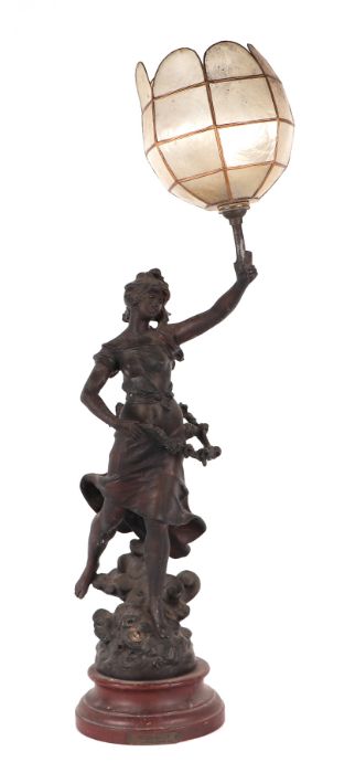 A spelter figural lamp in the form of a maiden holding a torch aloft, mounted on a wooden base,
