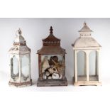 Three painted metal storm lanterns, one containing a collection of seashells, largest 53cms high (