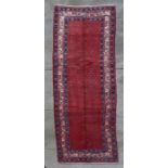 A Persian woollen hand knotted runner with repeating motifs within stylised borders, on a red