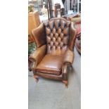 A brown leather upholstered wing back armchair in