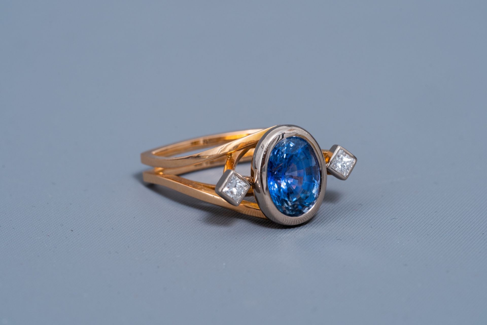 An 18 carat yellow and white gold ring set with a blue sapphire and two diamonds, 20th C.