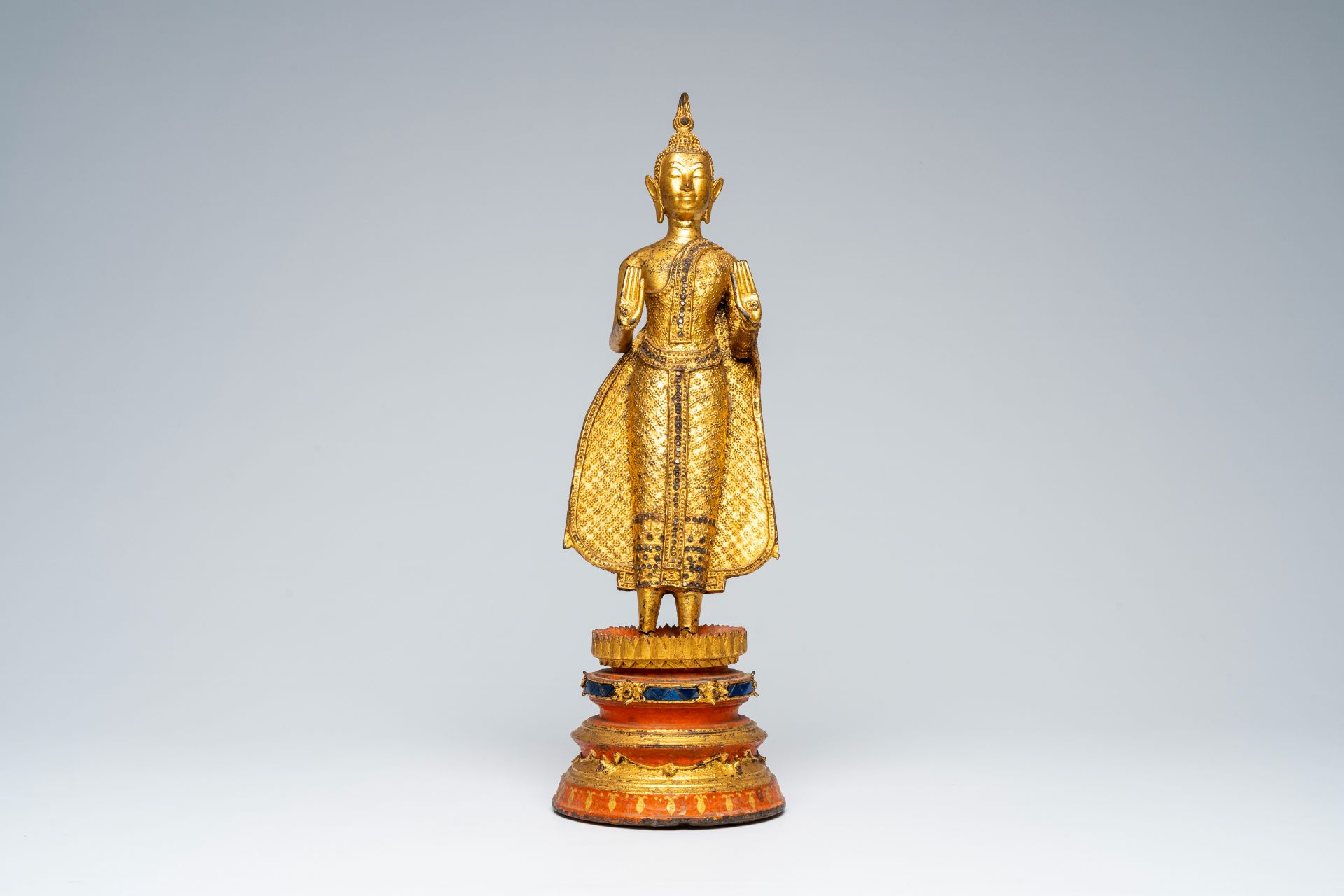 A Thai gilt bronze figure of a standing Buddha on a polychrome painted and glass inlaid metal base, - Image 2 of 8