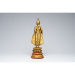 A Thai gilt bronze figure of a standing Buddha on a polychrome painted and glass inlaid metal base,