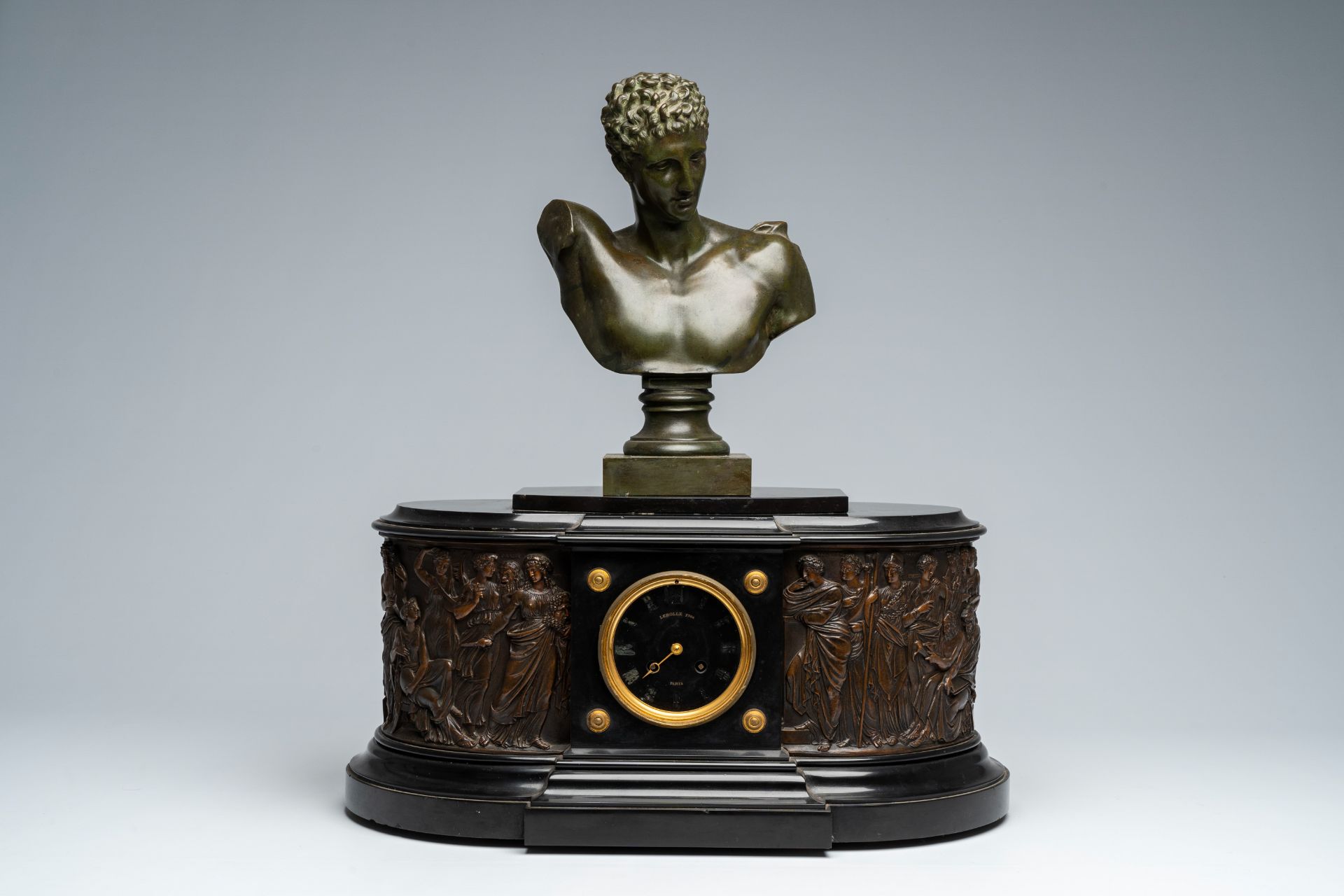 A French black marble mantel clock with a 'Greek goddesses' frieze surmounted by a patinated bronze