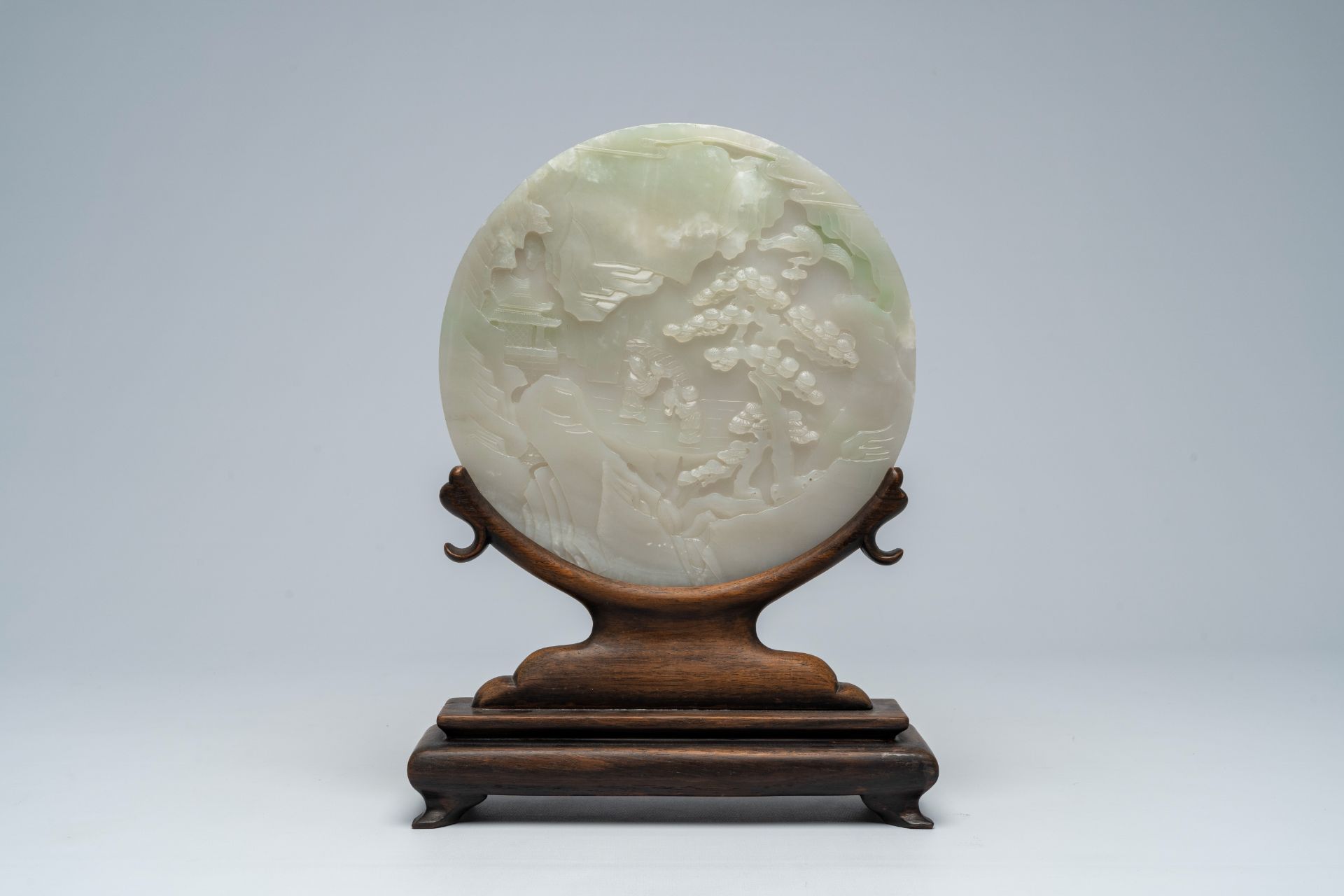 A large Chinese white jade plaque with figures in a landscape on a wooden stand, 19th/20th C