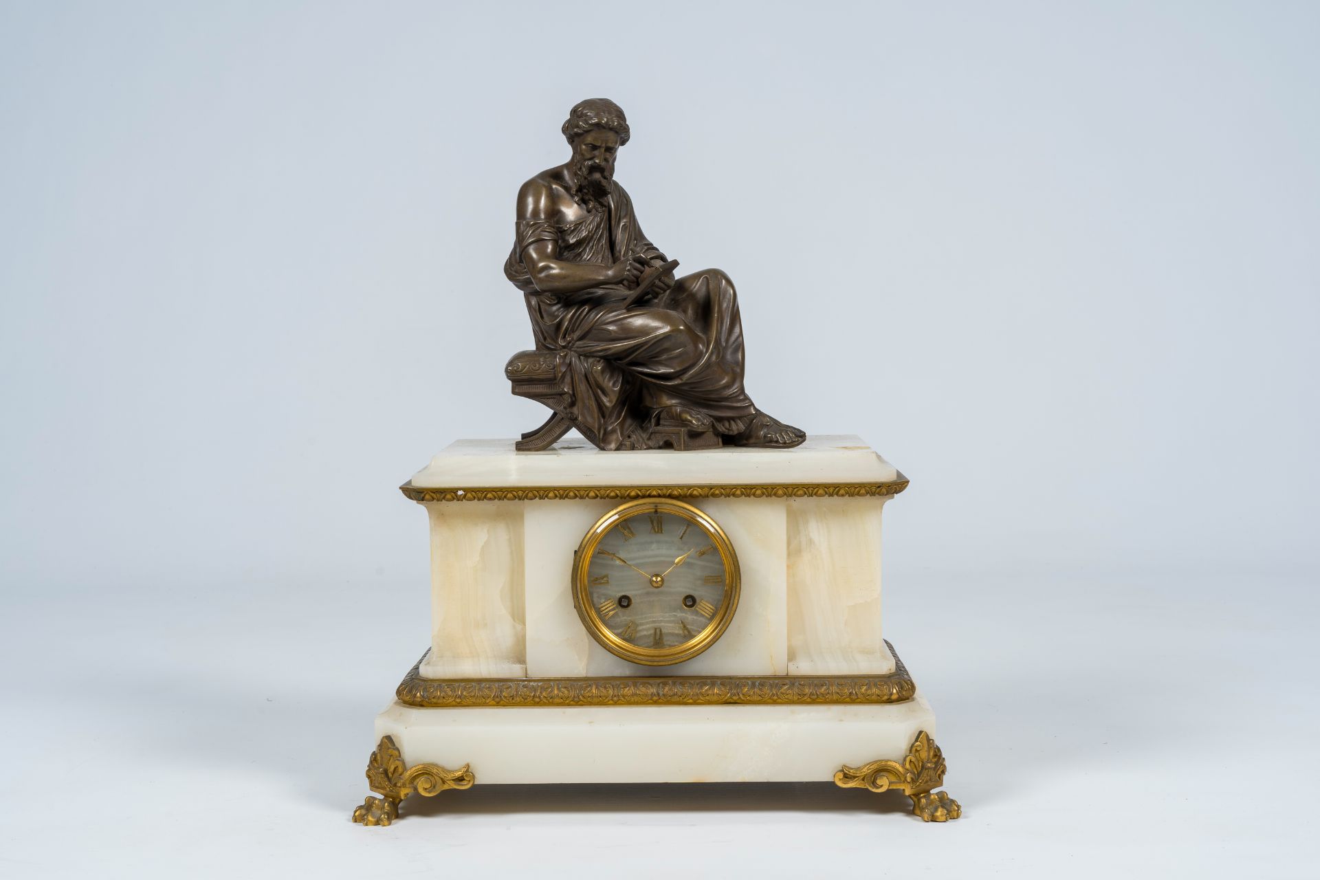 A French gilt and patinated bronze mounted white onyx mantel clock with a legist, 19th C.