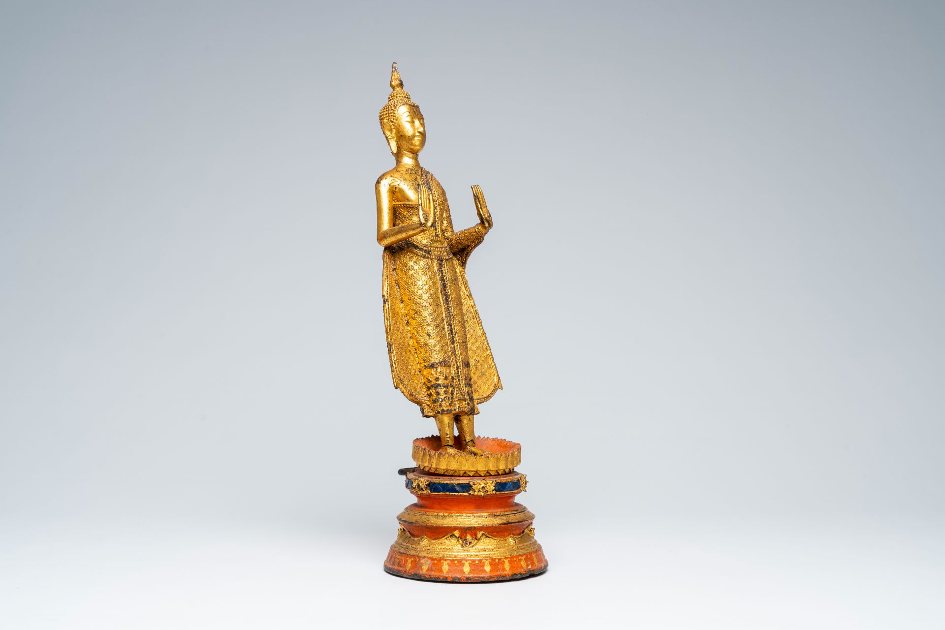 A Thai gilt bronze figure of a standing Buddha on a polychrome painted and glass inlaid metal base, - Image 6 of 8