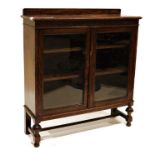 20th century oak display cabinet with two glazed doors enclosing shelves, on turned and block