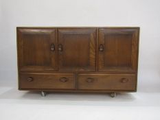 Ercol elm sideboard with oval dished handles, 3 cupboard doors above 2 drawers on casters (129cm