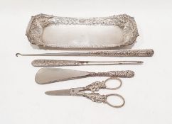 Silver-coloured tray with embossed scrolling and scallop decoration, a silver-handled button hook, a