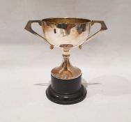 Foreign silver coloured metal two-handled trophy cup, circular with flattened handle, on wooden