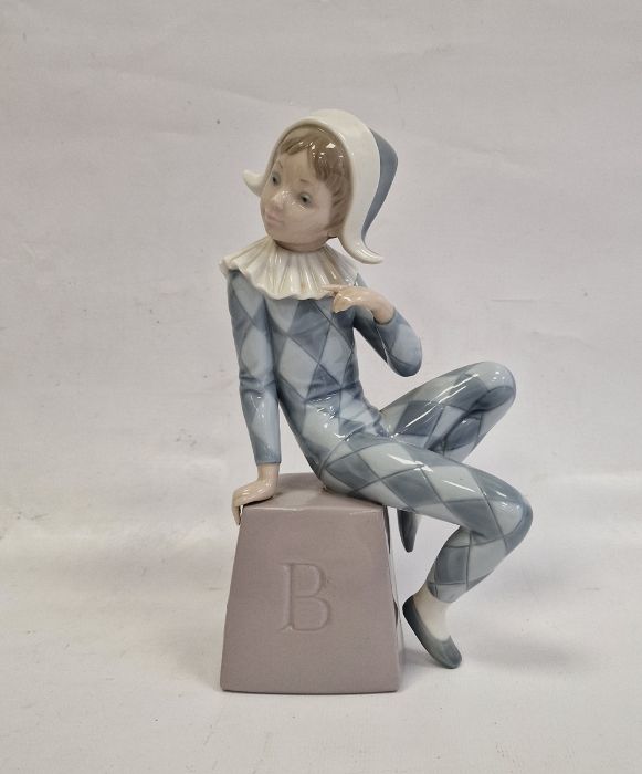 Lladro figure of boy wearing harlequin suit seated on box initialled B, 20.5cm high