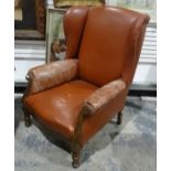 Early 20th century wingback armchair in brown leather upholstery, on turned front legs