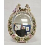 German late 19th century porcelain flower encrusted oval mirror, applied with two putti suspending a