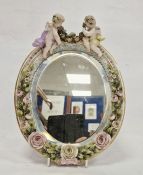 German late 19th century porcelain flower encrusted oval mirror, applied with two putti suspending a